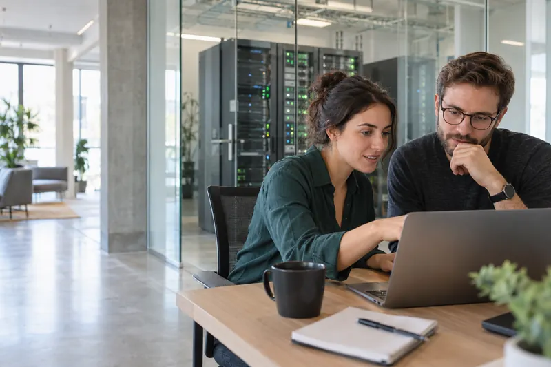 Two professionals collaborating beside a server room, illustrative scene.